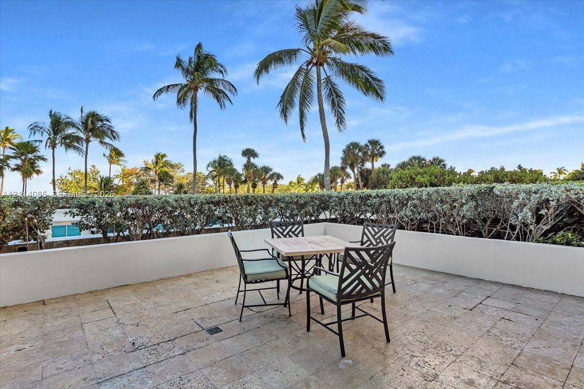 Elevated terrace featuring natural stone flooring, low-profile concrete perimeter walls, and manicured hedge screening with palm trees