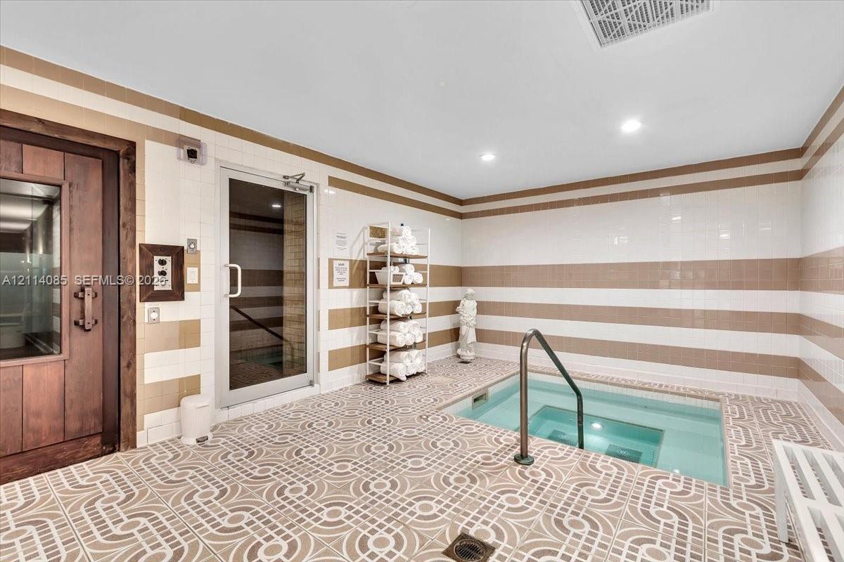 Spa area featuring an inground plunge pool with a metal handrail, enclosed glass-door steam room, wood-framed sauna door, and decorative tile flooring