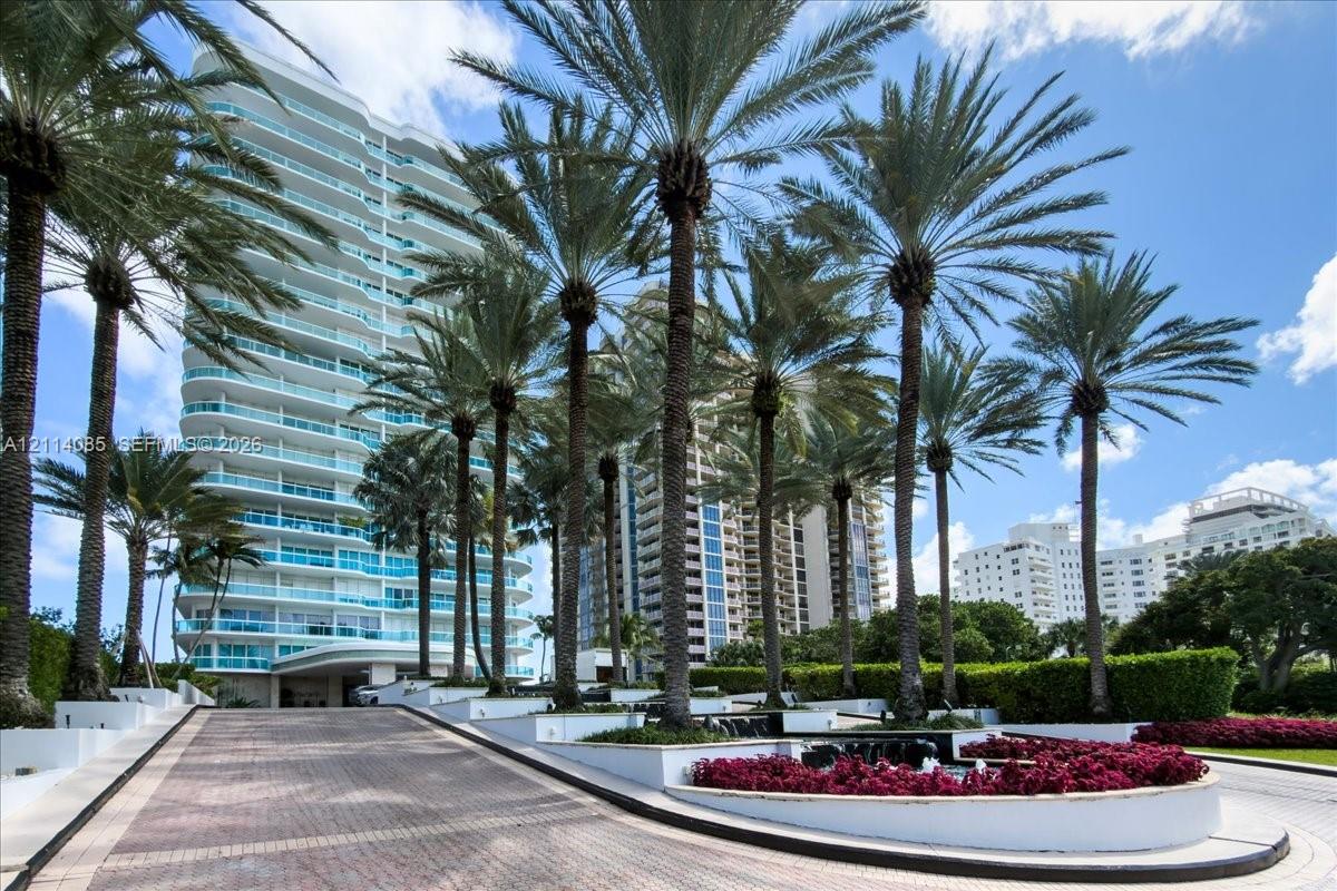 High-rise residential exterior featuring a paved drive, mature palm tree landscaping, tiered concrete planters, and integrated greenery