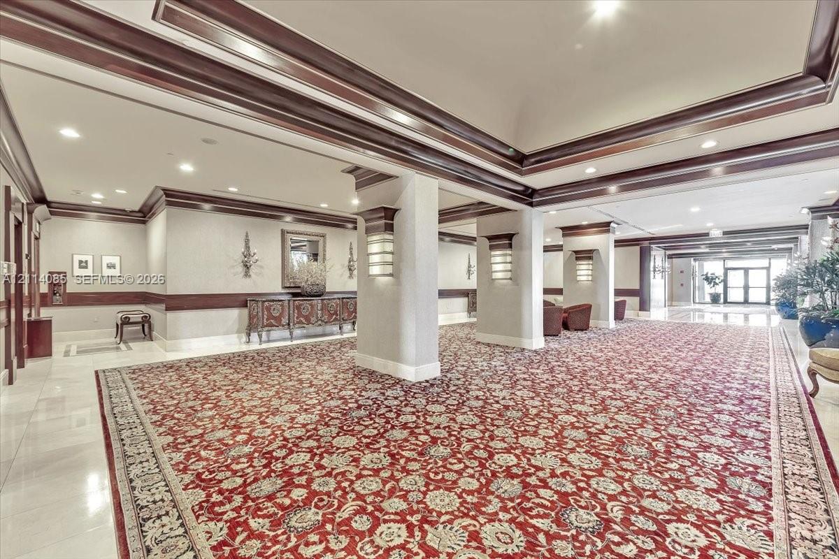 Grand lobby featuring coffered ceilings, crown molding, decorative millwork, columned pillars, and wall-mounted sconce lighting