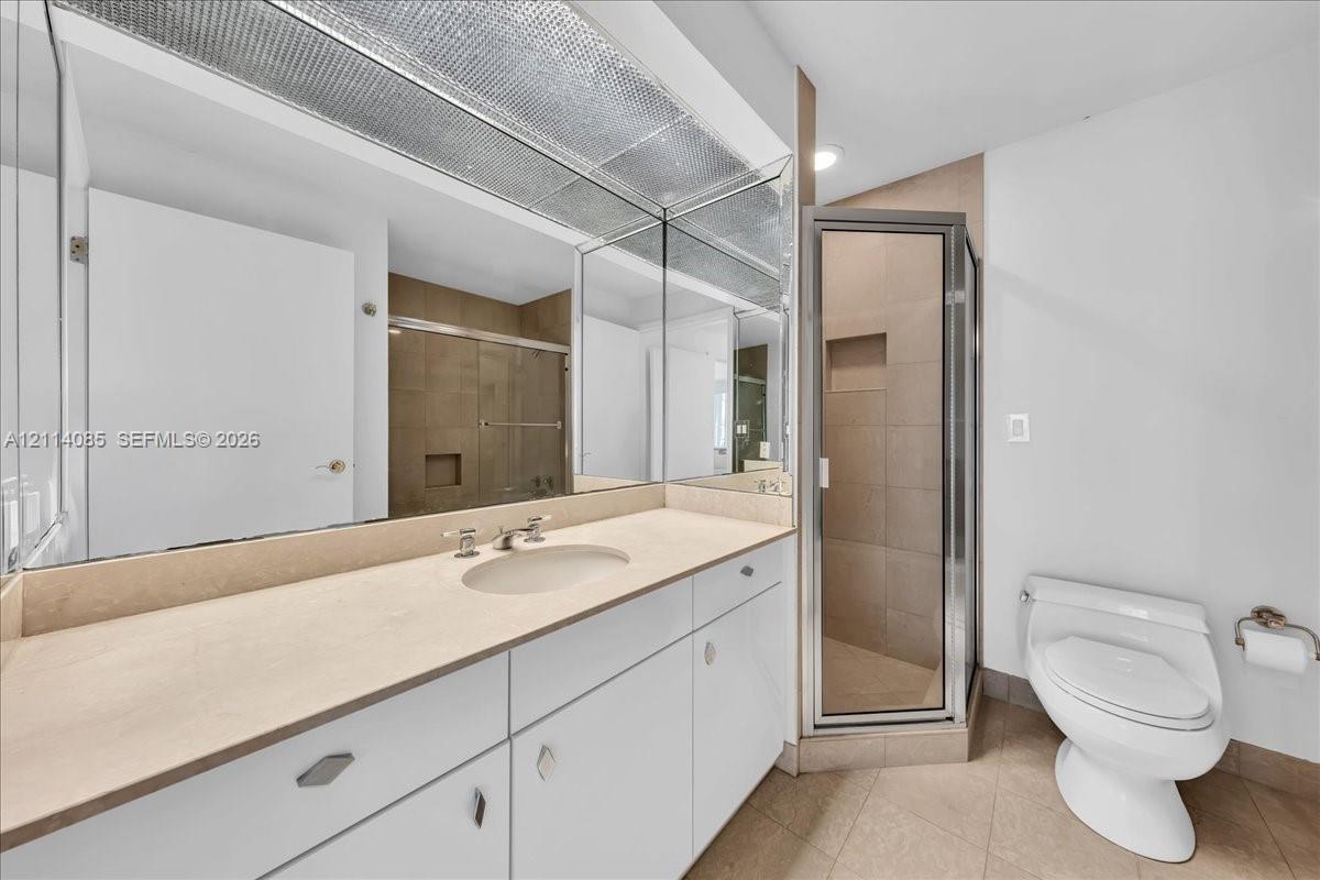 Bathroom featuring white cabinetry, solid-surface countertop, full-width mirror, and a glass-enclosed shower with tile surround