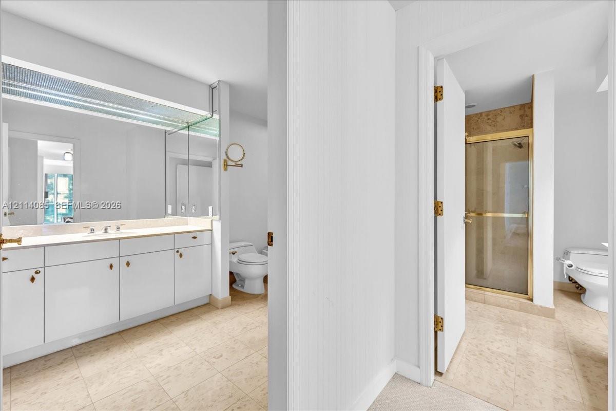 Bathroom featuring white cabinetry, full-width mirror, stone-finish flooring, glass-enclosed shower, and built-in vanity lighting