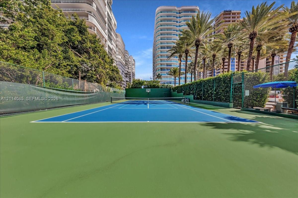 Private tennis court featuring a hard-surface surface, chain-link perimeter fencing, and mature perimeter landscaping