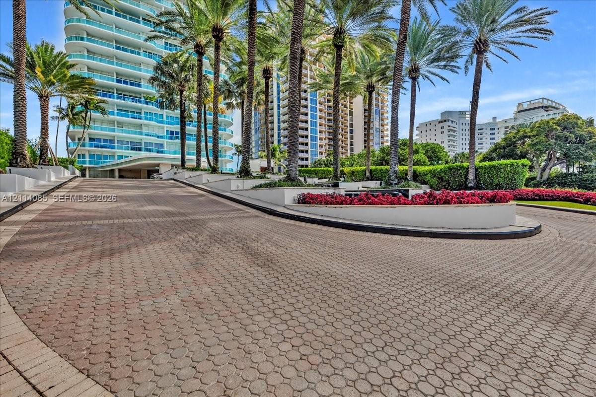 Paver stone driveway featuring manicured perimeter landscaping, elevated concrete planters, and mature palm trees