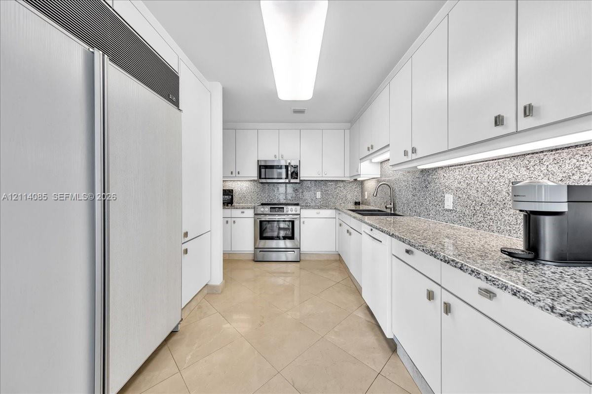 Kitchen featuring white cabinetry, stone-finish countertops, stainless steel appliances, under-cabinet lighting, and tile flooring