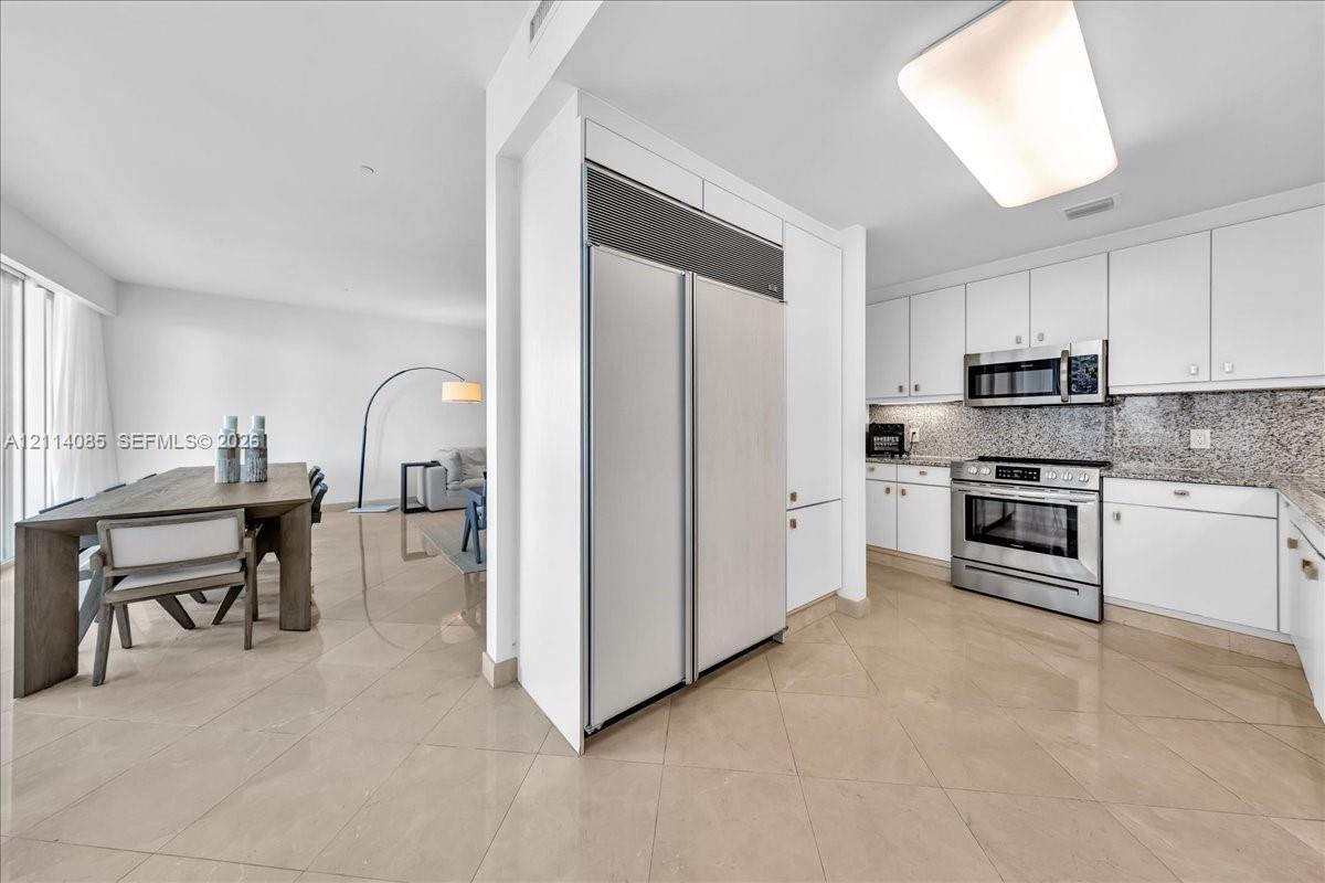 Kitchen featuring white cabinetry, stone countertops, stainless steel appliances, and large-format tile flooring