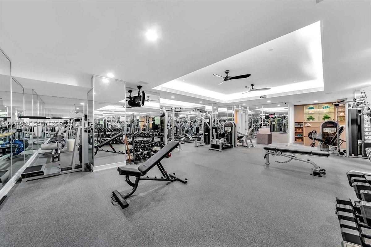 Fitness facility featuring floor-to-ceiling mirrors, recessed tray ceiling, integrated ceiling fans, and rubberized flooring