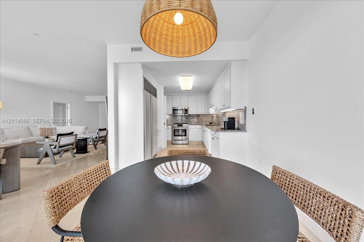 Kitchen featuring stainless steel appliances, white cabinetry, solid surface countertops, tile backsplash, and oversized dome pendant lighting