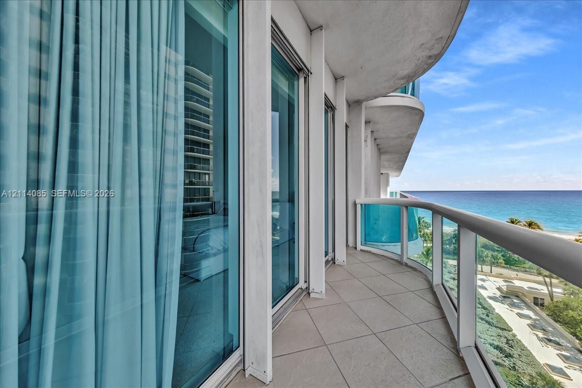 Curved private balcony featuring large-format tile flooring, glass panel railings, and floor-to-ceiling sliding glass doors