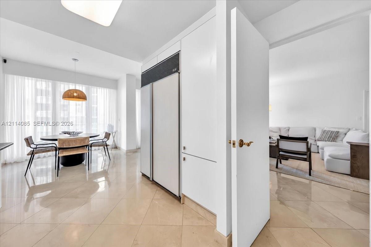 High-gloss stone flooring, floor-to-ceiling drapery, built-in panel-ready refrigeration, and minimalist flat-panel cabinetry
