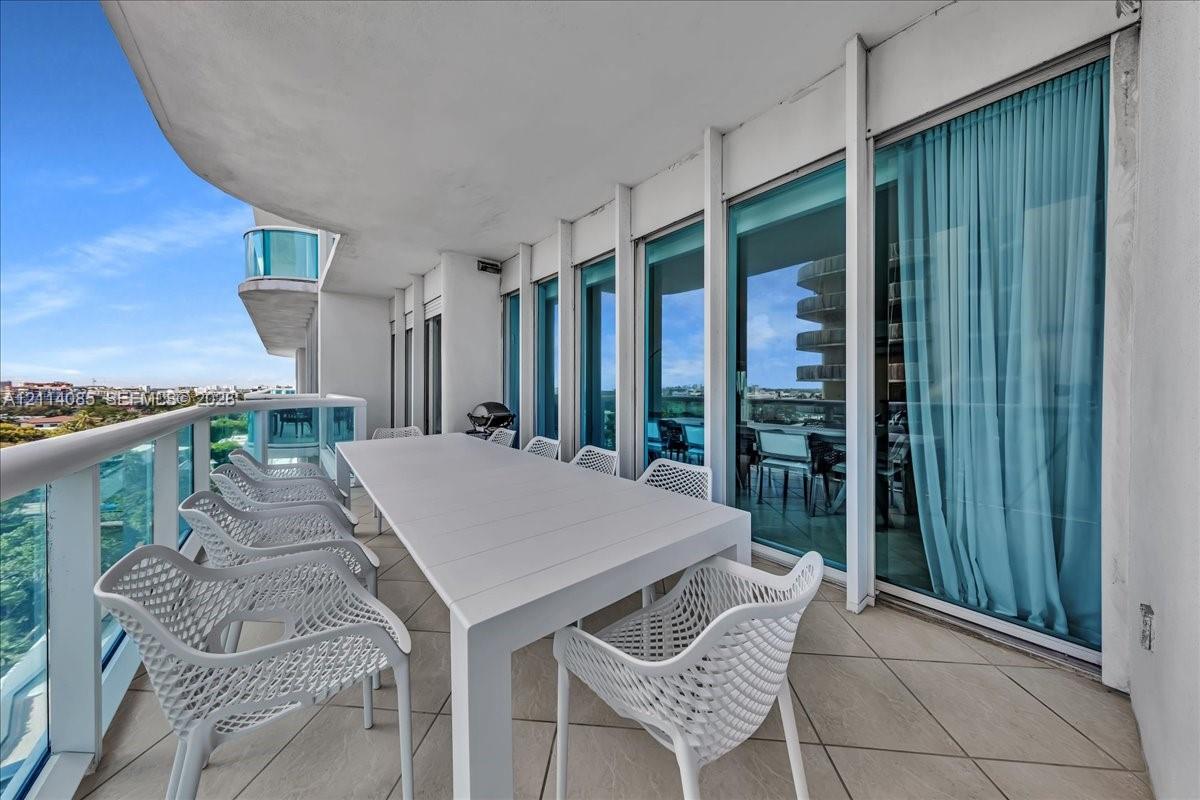 Expansive covered balcony with large-format tile flooring, glass panel railings, and floor-to-ceiling glass doors