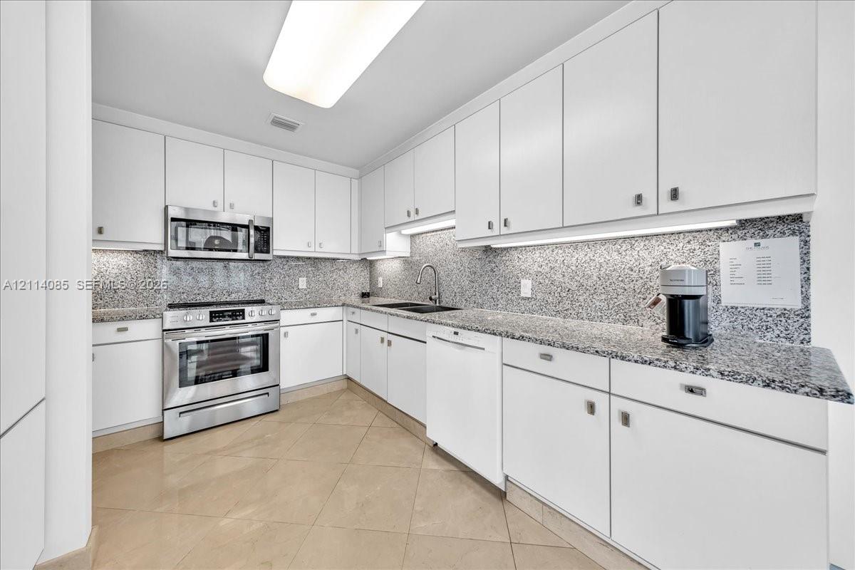 Kitchen featuring white cabinetry, stone-finish countertops, full-height backsplash, stainless steel appliances, and tile flooring