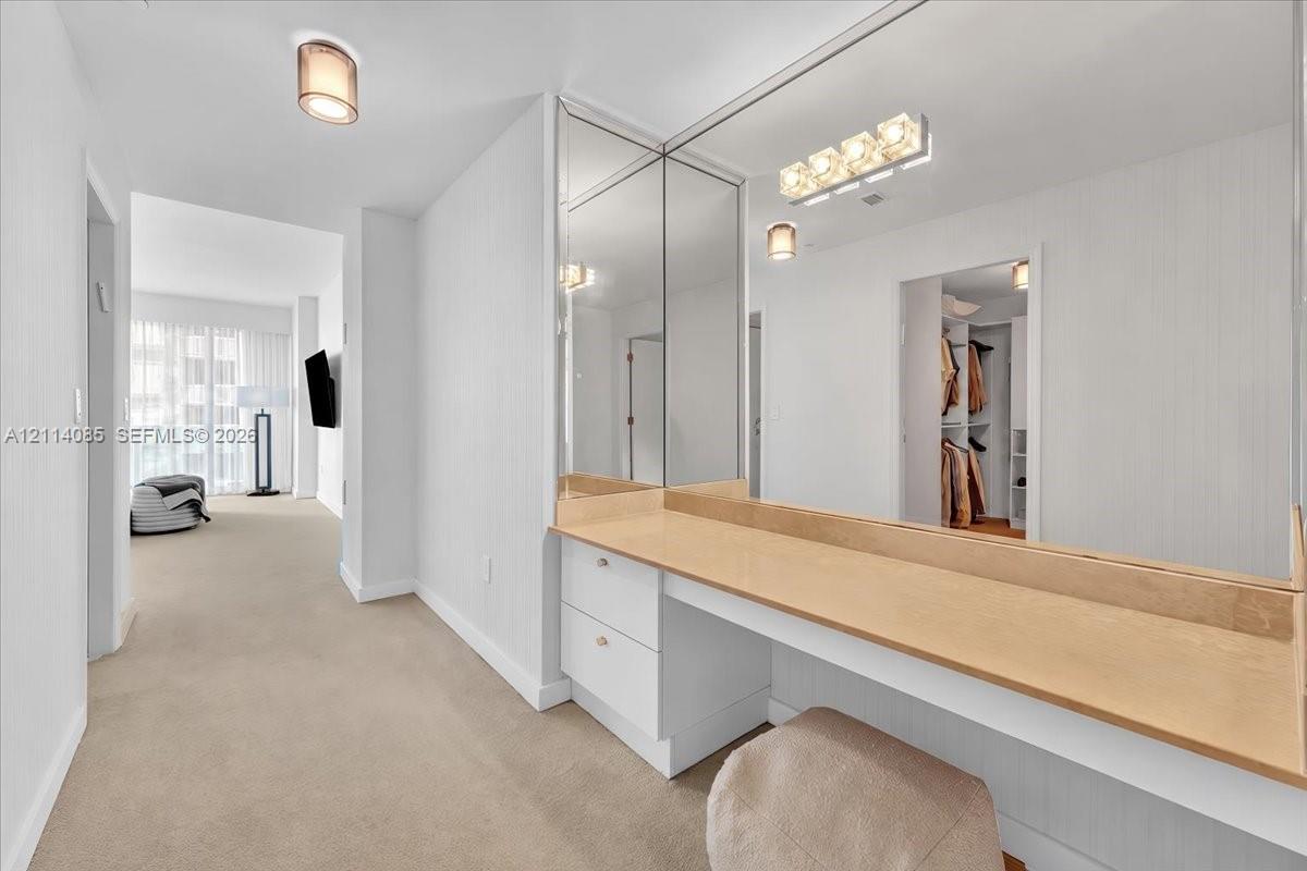 Built-in vanity featuring a light-toned countertop, white cabinetry with drawer storage, full-length mirror paneling, and wall-mounted light fixtures
