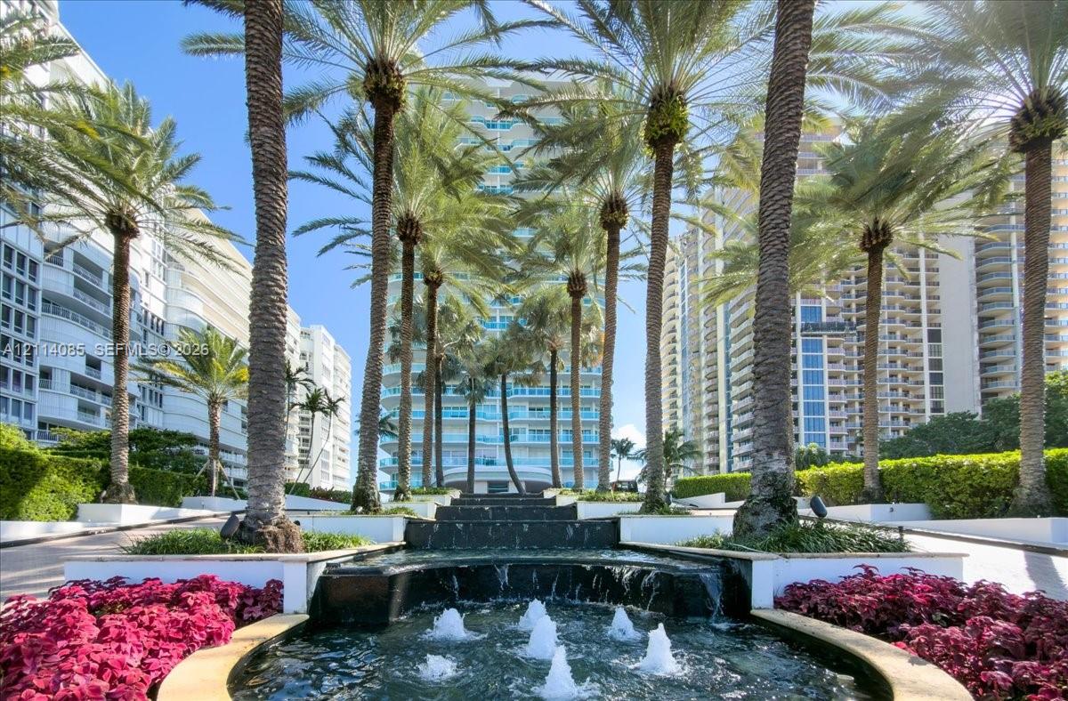 Tiered stone water feature, mature palm trees, and manicured landscaping with floral beds