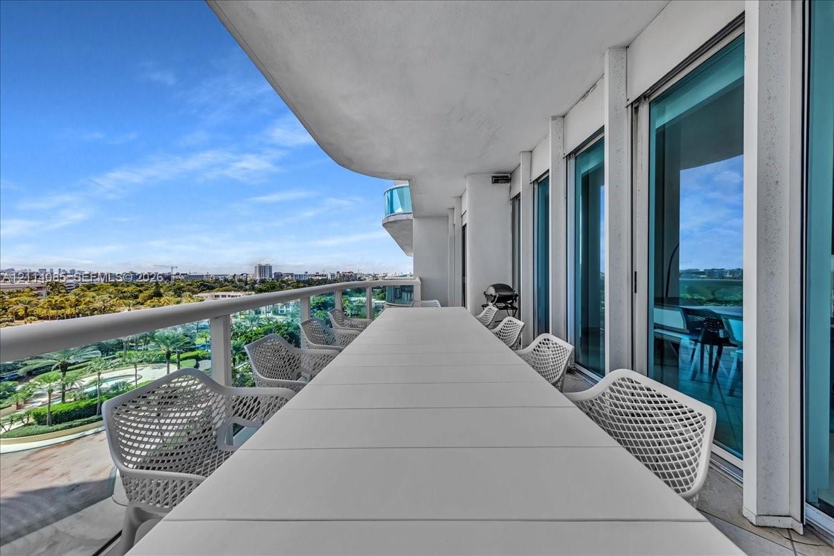 Covered balcony featuring a wrap-around glass railing and tile flooring, accessible via floor-to-ceiling sliding glass doors