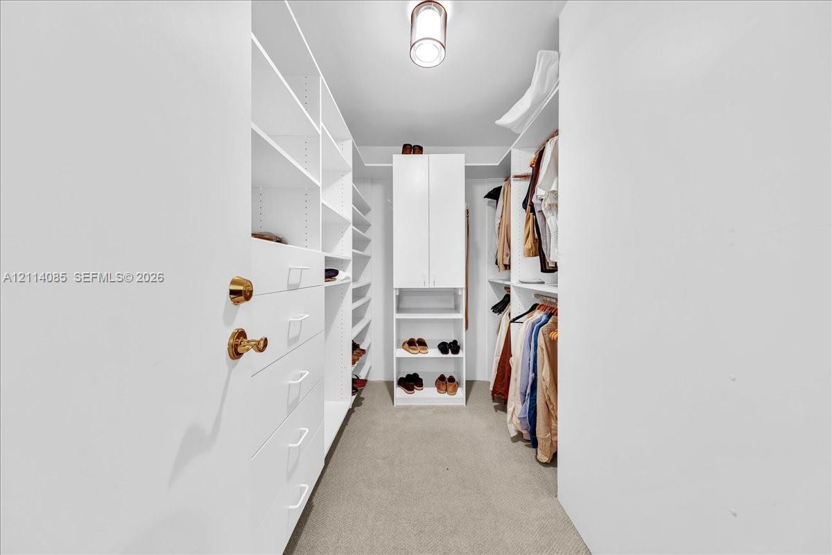 Walk-in storage space featuring built-in white cabinetry, multiple shelving units, integrated drawer storage, and overhead pendant lighting