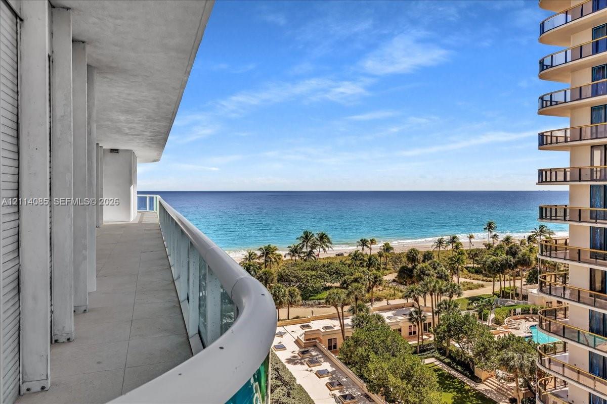 Expansive covered balcony featuring tile flooring and a glass railing, overlooking the coastline and ocean horizon