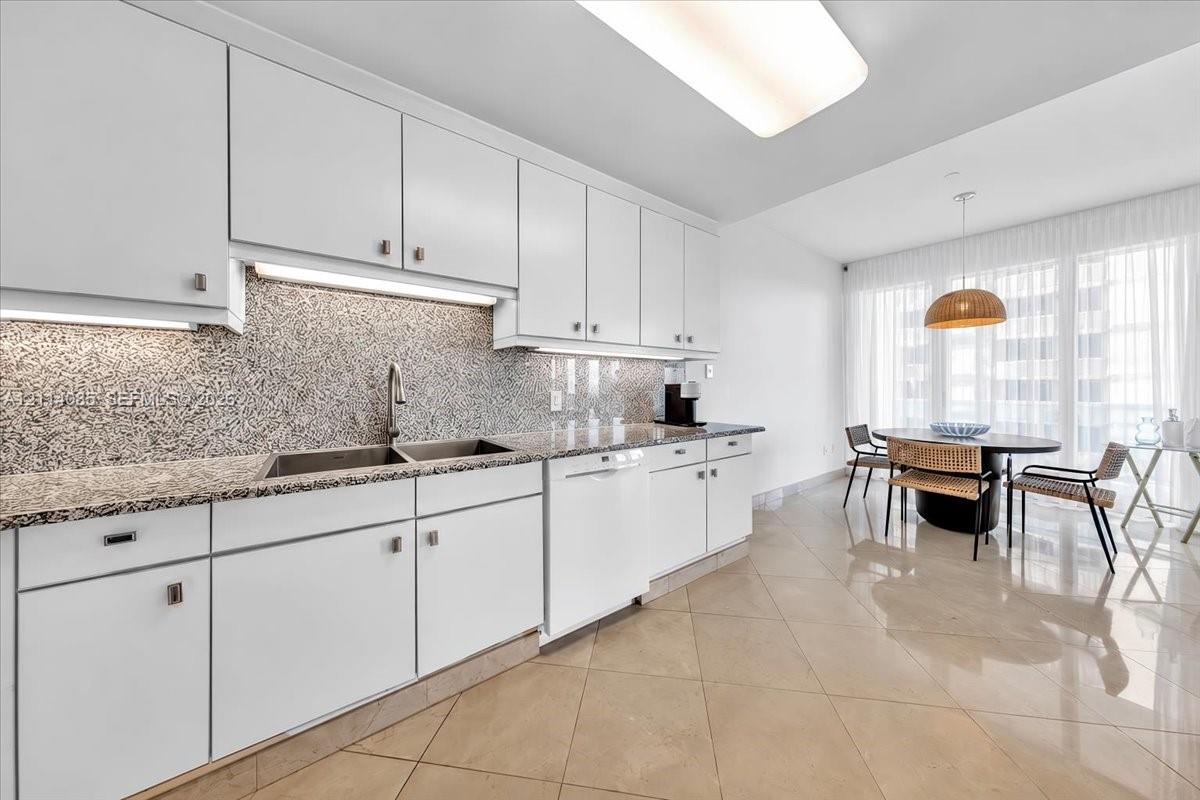 Kitchen featuring white cabinetry, stone-finish countertops, full-height stone-finish backsplash, stainless steel dual-basin sink, and polished tile flooring
