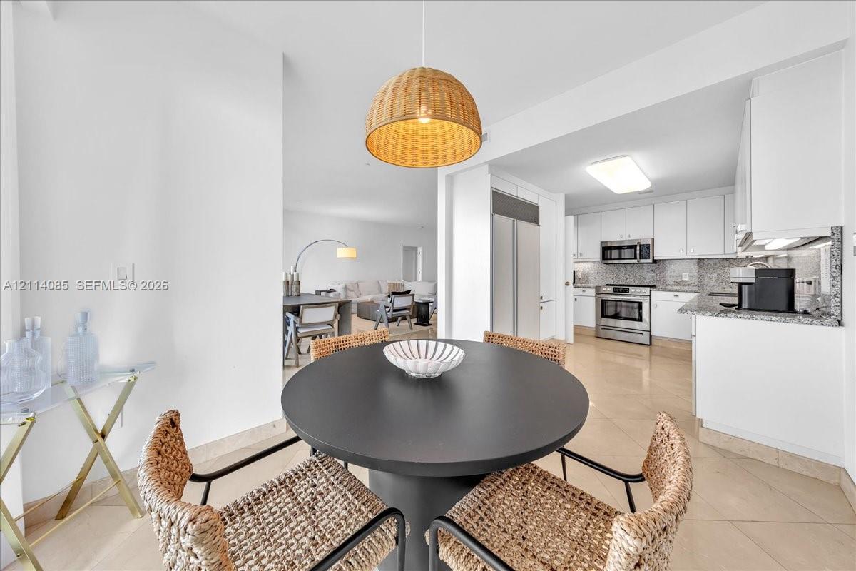 Kitchen featuring white cabinetry, stone countertops, and stainless steel appliances, complemented by large-format tile flooring and a woven pendant light fixture