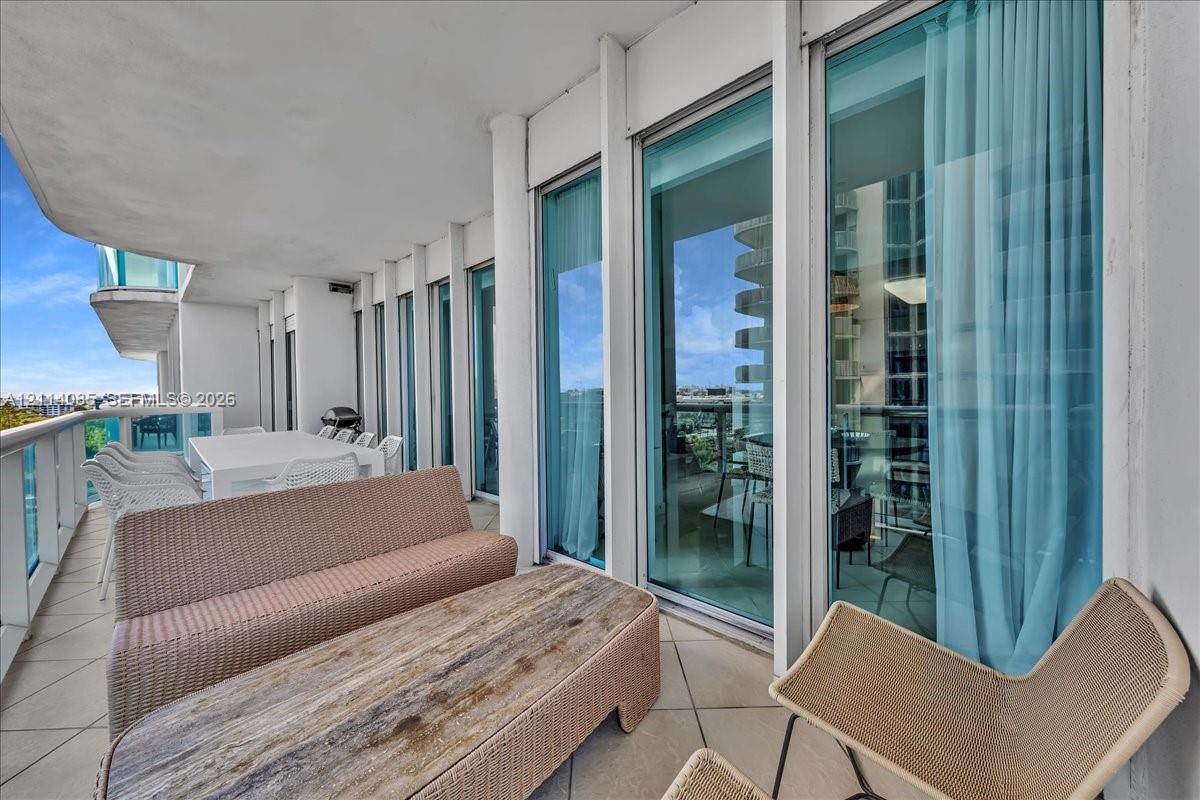 Expansive covered balcony featuring large-format tile flooring, vertical structural columns, and full-height glass sliding doors