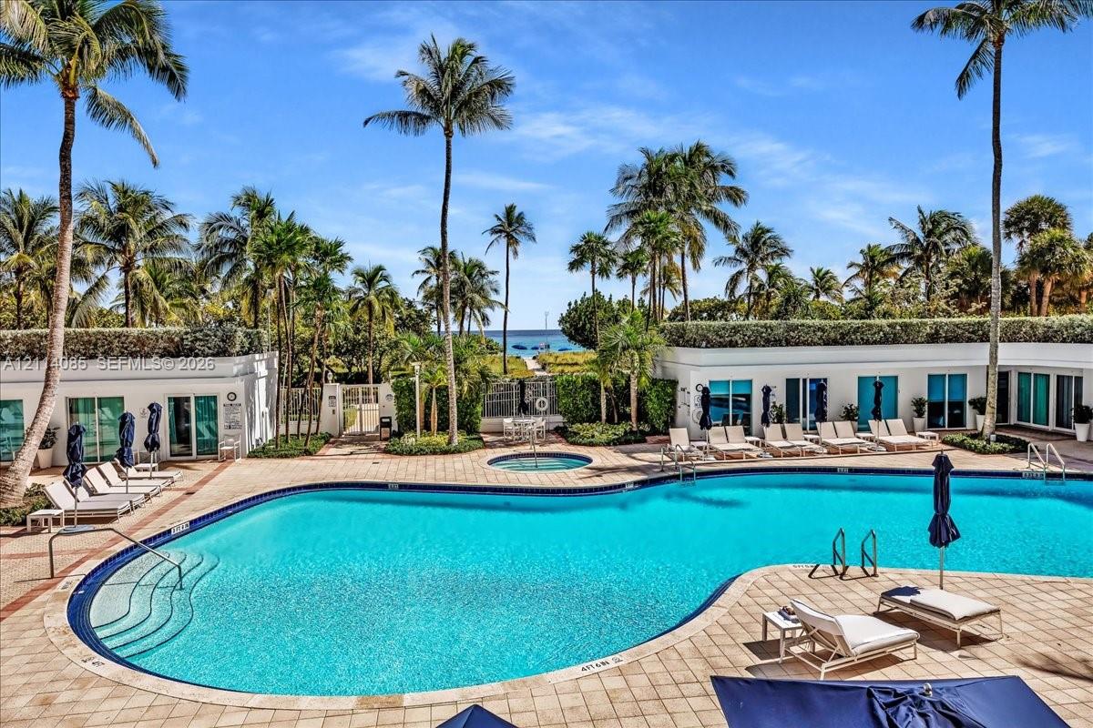 Resort-style pool area featuring a curved swimming pool, integrated spa, paved terrace, and mature palm trees