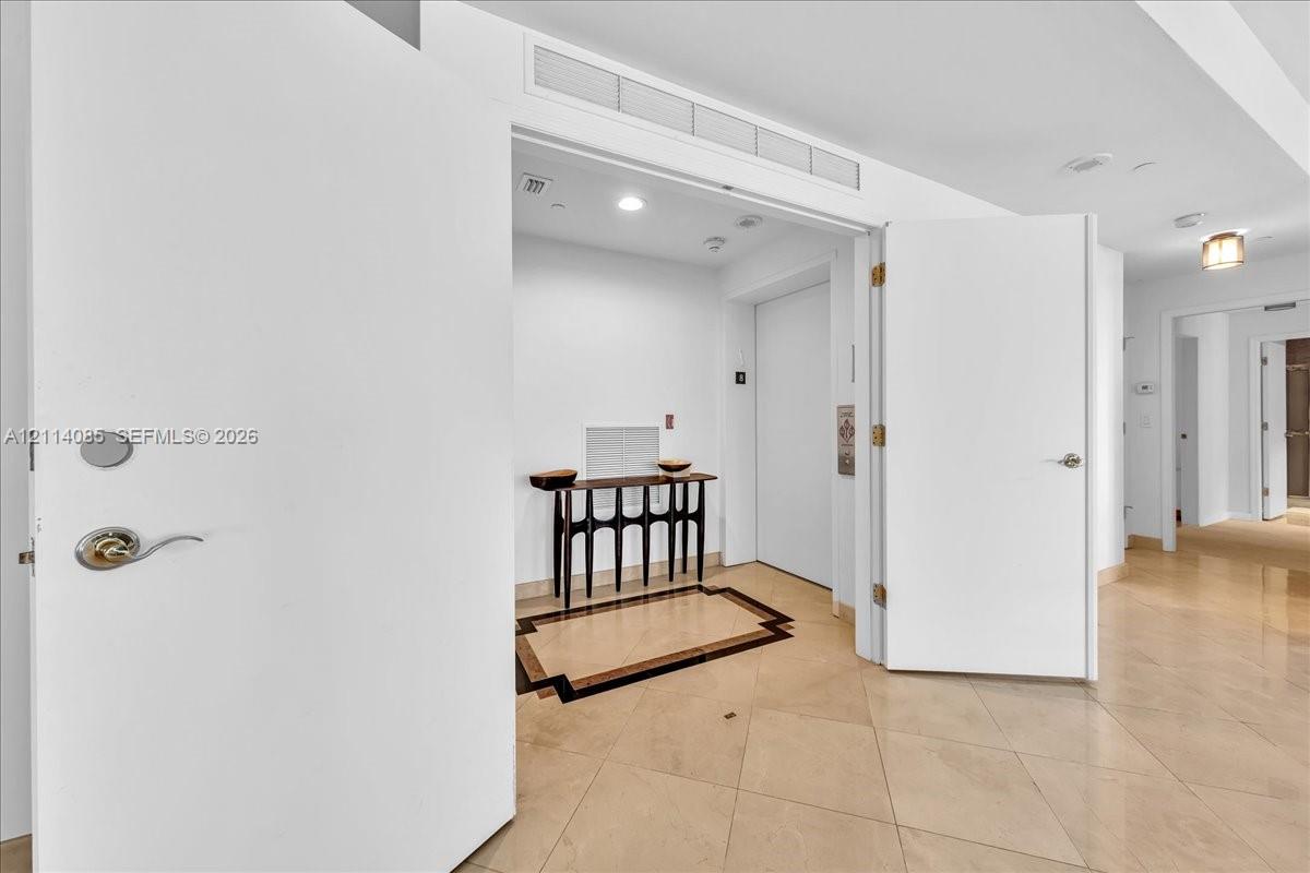 Neutral tile flooring featuring a decorative inlaid border, double door entry, and recessed lighting