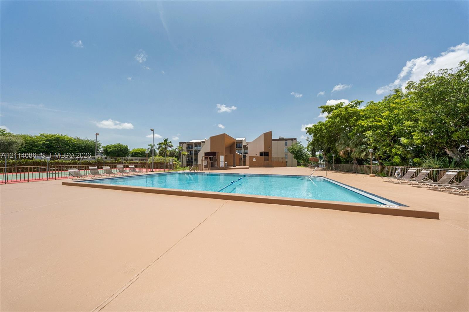 Swimming pool featuring a concrete deck, metal perimeter fencing, and surrounding mature trees
