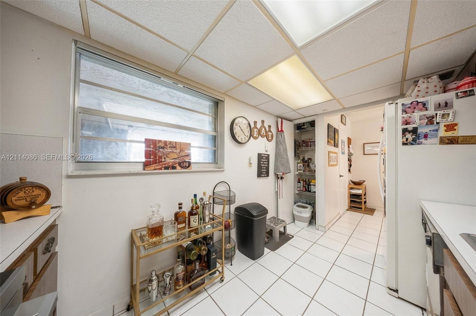 Kitchen featuring white tile flooring, drop ceiling with integrated lighting, slider window, and built-in pantry cabinetry