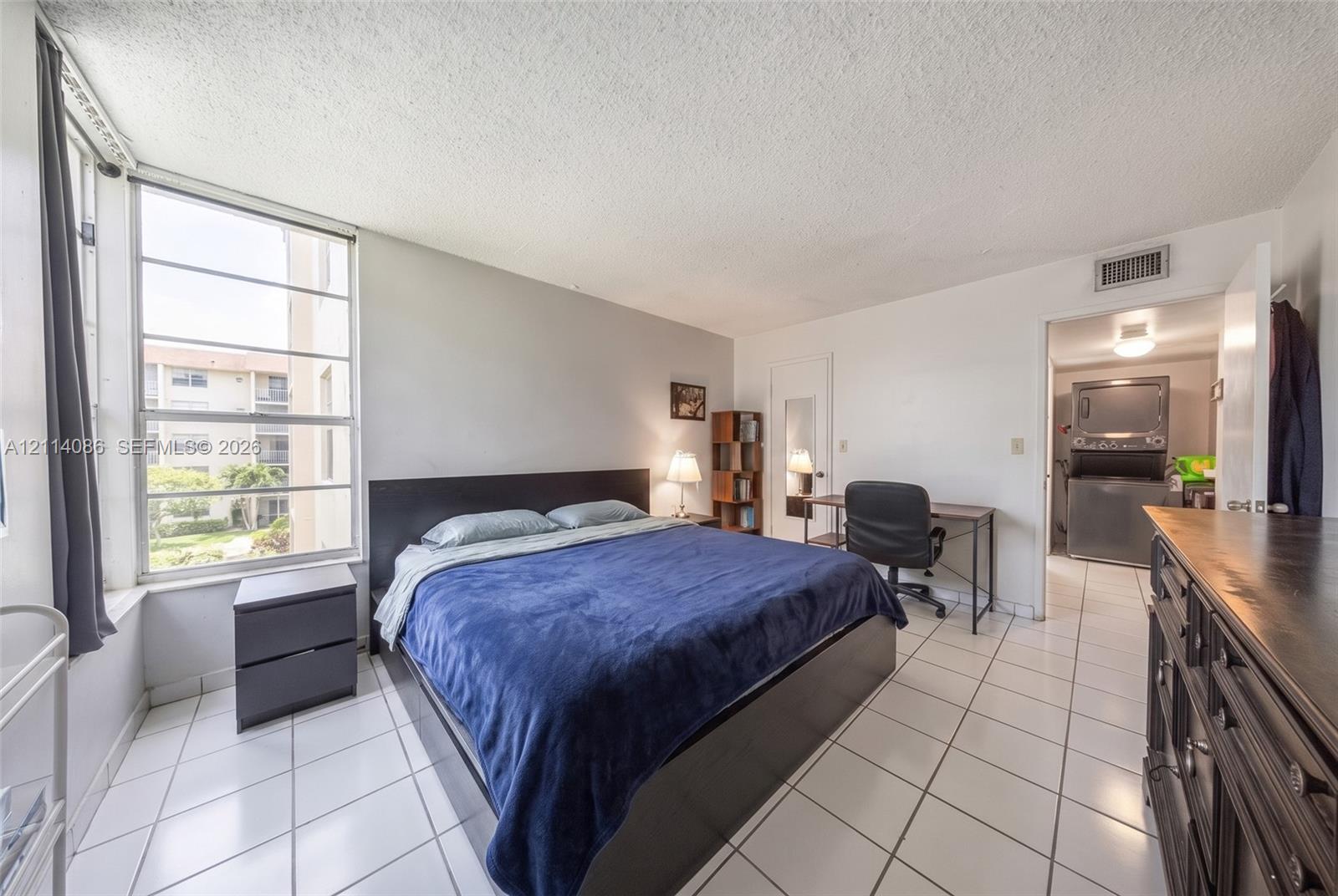 Large format window with grid detailing, ceramic tile flooring, and dedicated laundry area featuring a stacked washer and dryer