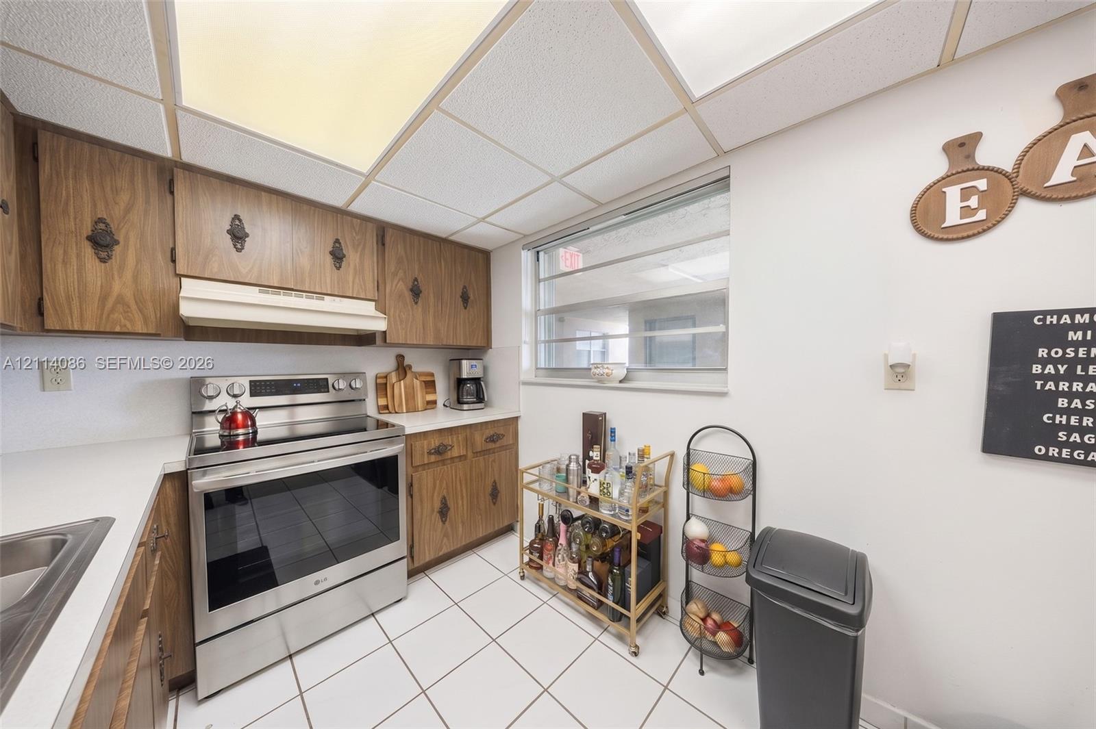 Kitchen featuring wood cabinetry, stainless steel range with overhead vent hood, ceramic tile flooring, and integrated drop-in sink