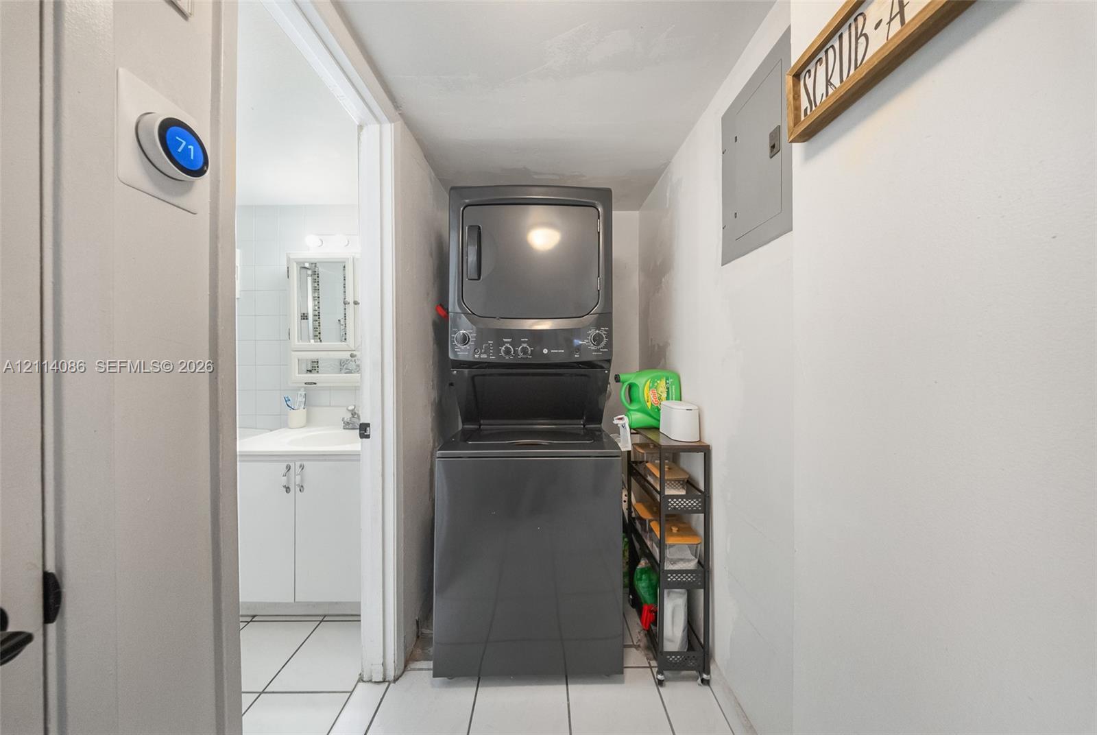 Laundry area featuring a stackable washer and dryer, tile flooring, and a wall-mounted programmable thermostat