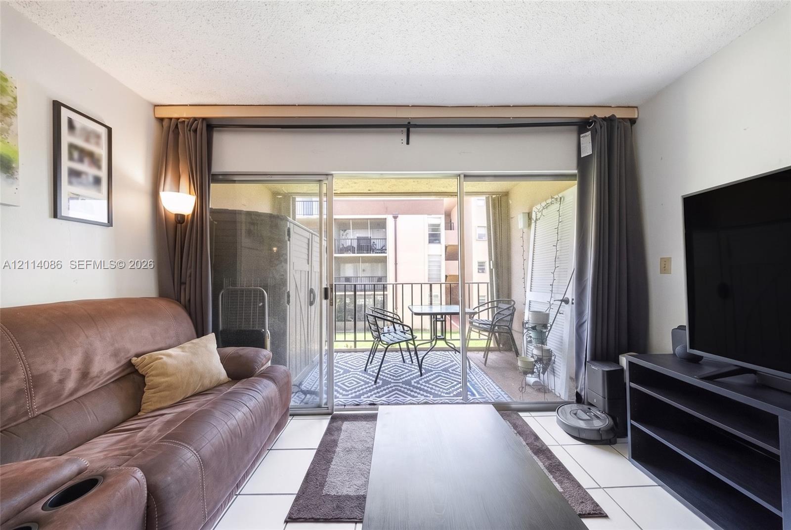 Living area featuring large format tile flooring and floor-to-ceiling sliding glass doors opening to a private balcony with metal railing