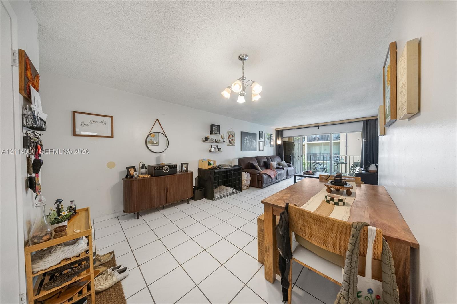 Open-concept room featuring white ceramic tile flooring, a multi-arm chandelier, and sliding glass doors with direct exterior access