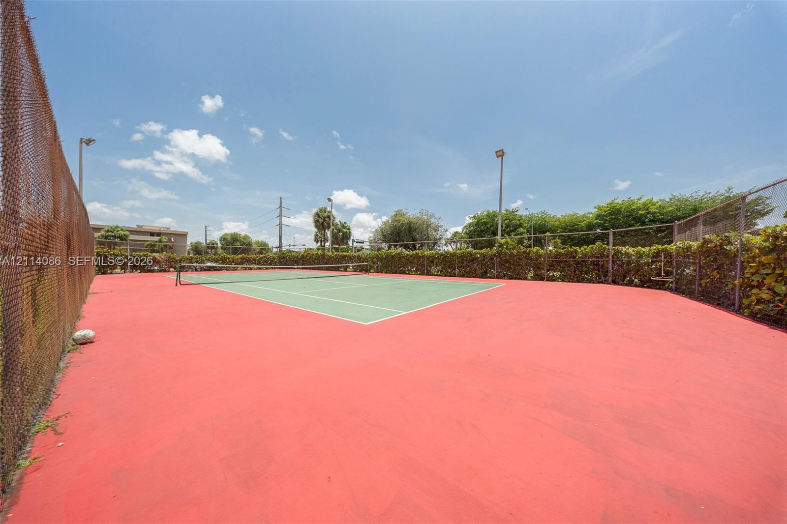 Private tennis court featuring a hard surface, perimeter chain-link fencing, and integrated lighting poles