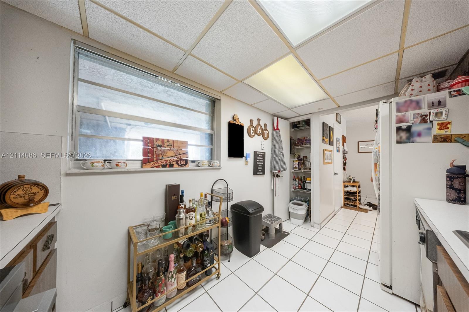 Kitchen featuring white tile flooring, drop ceiling panels, horizontal slider window, and built-in pantry storage