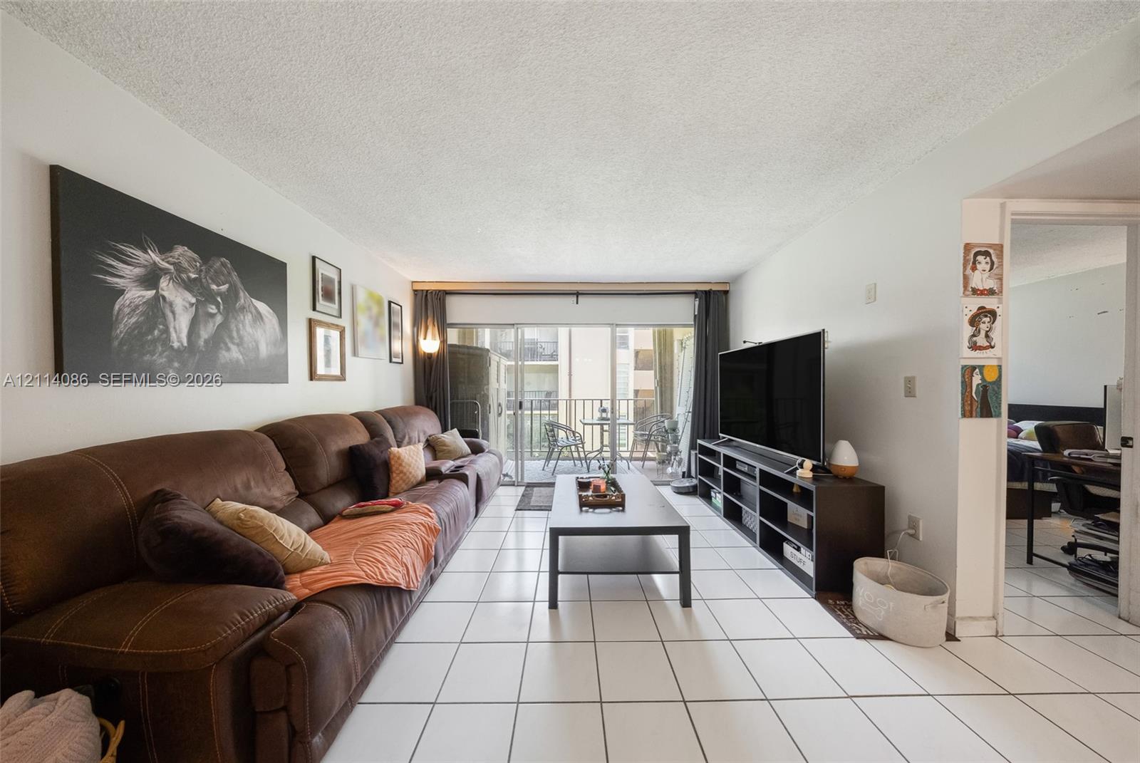 Living area featuring white ceramic tile flooring and sliding glass doors with access to an exterior balcony