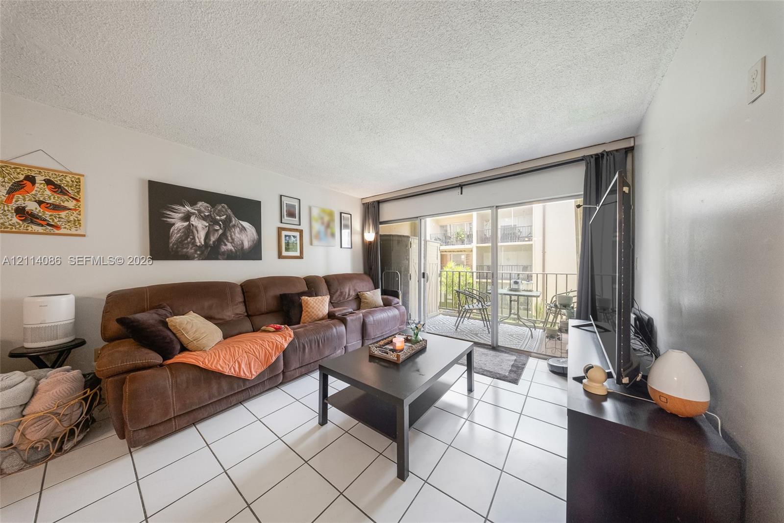 Living area featuring white ceramic tile flooring and sliding glass doors with access to an exterior balcony