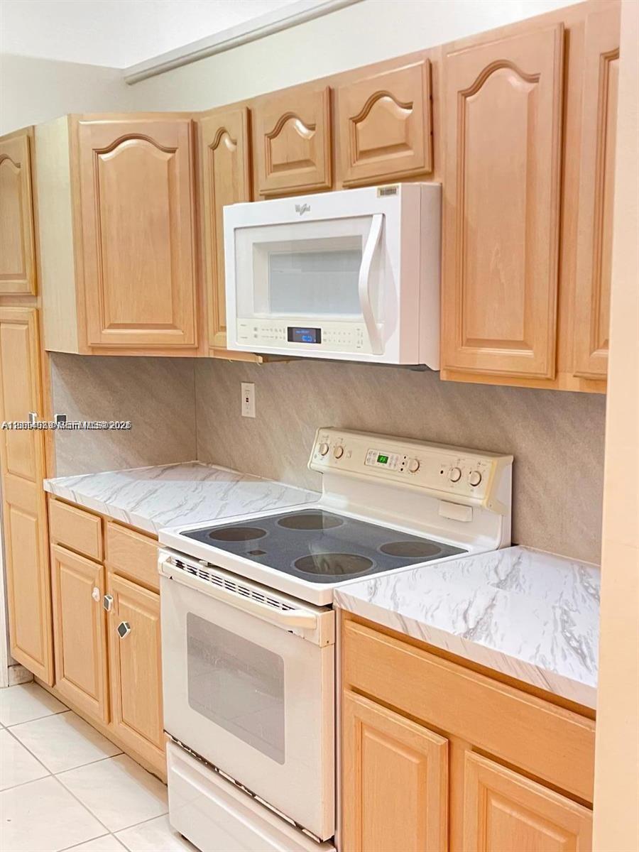 Kitchen featuring natural wood-finish cabinetry, stone-patterned laminate countertops, tile backsplash, and white appliance package Kitchen featuring natural wood-finish cabinetry, stone-patterned laminate countertops, tile backsplash, and white appliance package