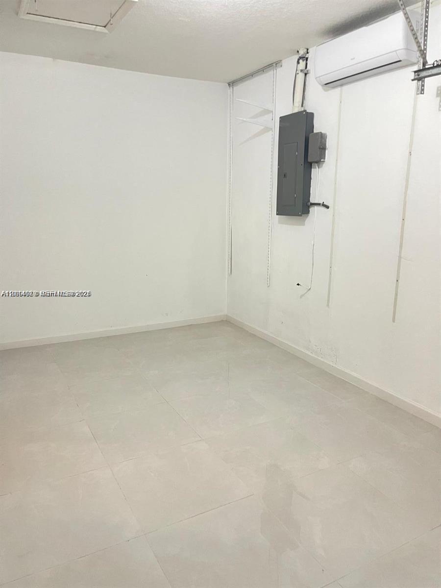 Enclosed space featuring large-format ceramic tile flooring, a mounted ductless mini-split climate control unit, and wall-mounted electrical panel Enclosed space featuring large-format ceramic tile flooring, a mounted ductless mini-split climate control unit, and wall-mounted electrical panel