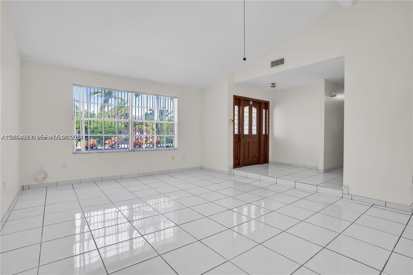 Vaulted ceilings, white ceramic tile flooring, large-format window with security bars, and a wooden entry door featuring glass inserts Vaulted ceilings, white ceramic tile flooring, large-format window with security bars, and a wooden entry door featuring glass inserts