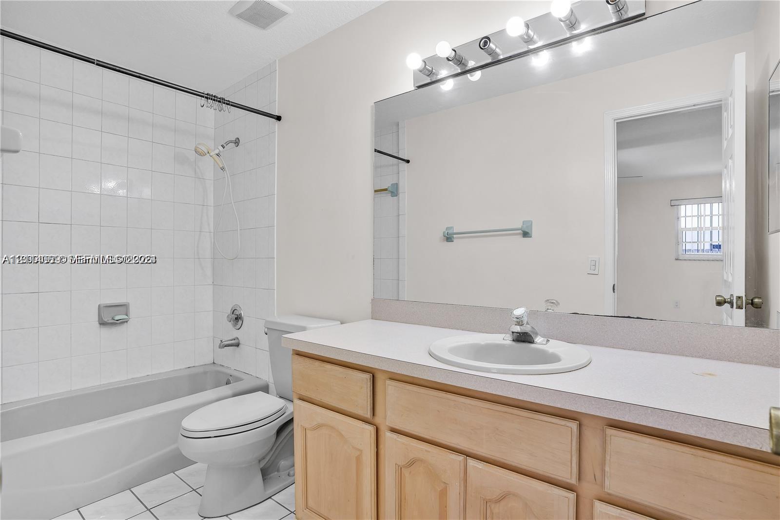 Bathroom featuring wood-finish cabinetry, a large wall-mounted vanity mirror, a drop-in sink, and a shower-tub combination with tiled surround Bathroom featuring wood-finish cabinetry, a large wall-mounted vanity mirror, a drop-in sink, and a shower-tub combination with tiled surround