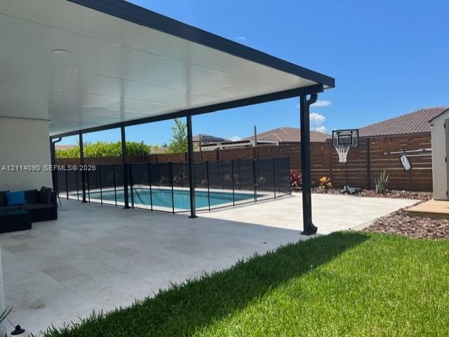 Covered patio featuring stone-finish pavers, recessed lighting, and a swimming pool with a black perimeter safety fence, set against horizontal slat privacy fencing Covered patio featuring stone-finish pavers, recessed lighting, and a swimming pool with a black perimeter safety fence, set against horizontal slat privacy fencing