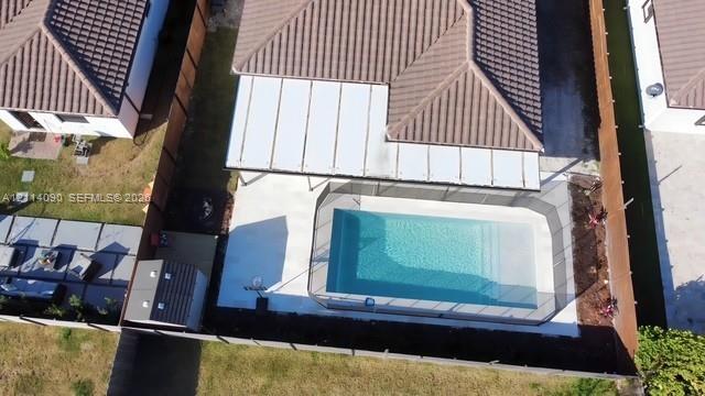 Aerial perspective of a backyard featuring a swimming pool with a surrounding mesh safety fence, a concrete patio, a covered pergola, and a storage shed, all enclosed by wood-panel fencing Aerial perspective of a backyard featuring a swimming pool with a surrounding mesh safety fence, a concrete patio, a covered pergola, and a storage shed, all enclosed by wood-panel fencing