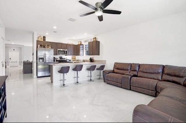 Open concept interior featuring polished tile flooring, dark wood-finish cabinetry, stainless steel appliances, a peninsula with stone-finish countertops, and a modern ceiling fan Open concept interior featuring polished tile flooring, dark wood-finish cabinetry, stainless steel appliances, a peninsula with stone-finish countertops, and a modern ceiling fan