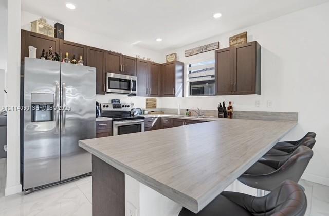 Kitchen featuring dark wood cabinetry, stainless steel appliances, wood-finish breakfast bar, and light-toned tile flooring Kitchen featuring dark wood cabinetry, stainless steel appliances, wood-finish breakfast bar, and light-toned tile flooring