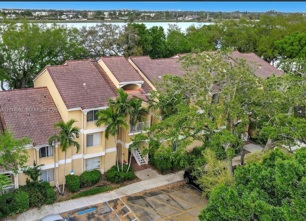 Multi-story residential building featuring a tile roof, stucco exterior, private balconies, and mature landscaping, situated along a waterfront