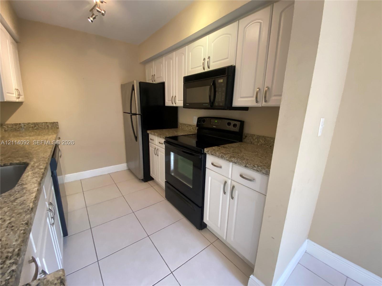 Kitchen featuring white cabinetry, stone-finish countertops, tile flooring, and integrated black appliances