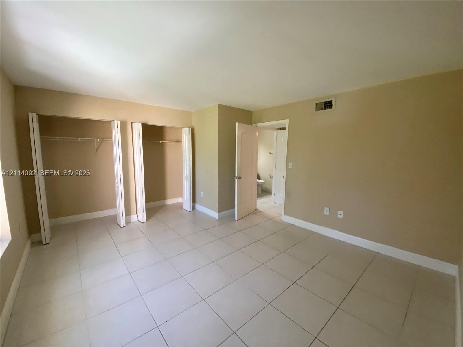 Room featuring large-format tile flooring, dual reach-in closets with bi-fold doors, and neutral wall color