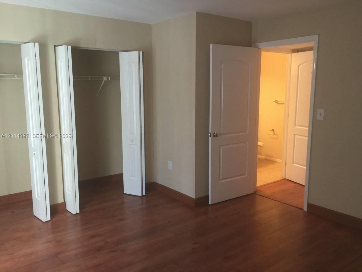 Room featuring wood-finish flooring, two sets of bifold closet doors with built-in shelving, and two interior doors with molded panel detailing