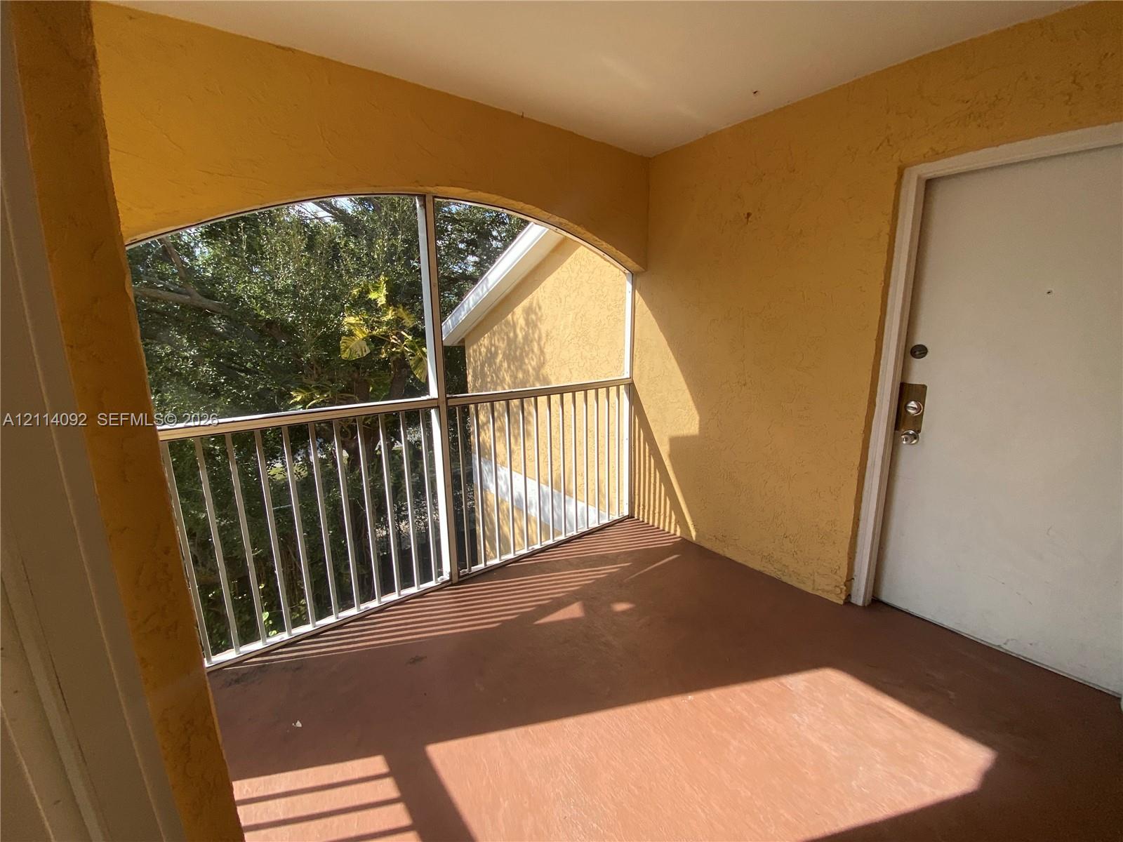 Covered balcony featuring an arched entryway, metal railing, screen enclosure, and solid surface flooring